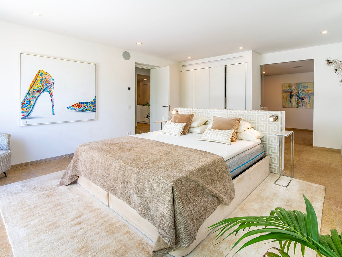 Chambre parentale moderne avec grand lit, sol en pierre naturelle, armoires intégrées et art mural coloré.