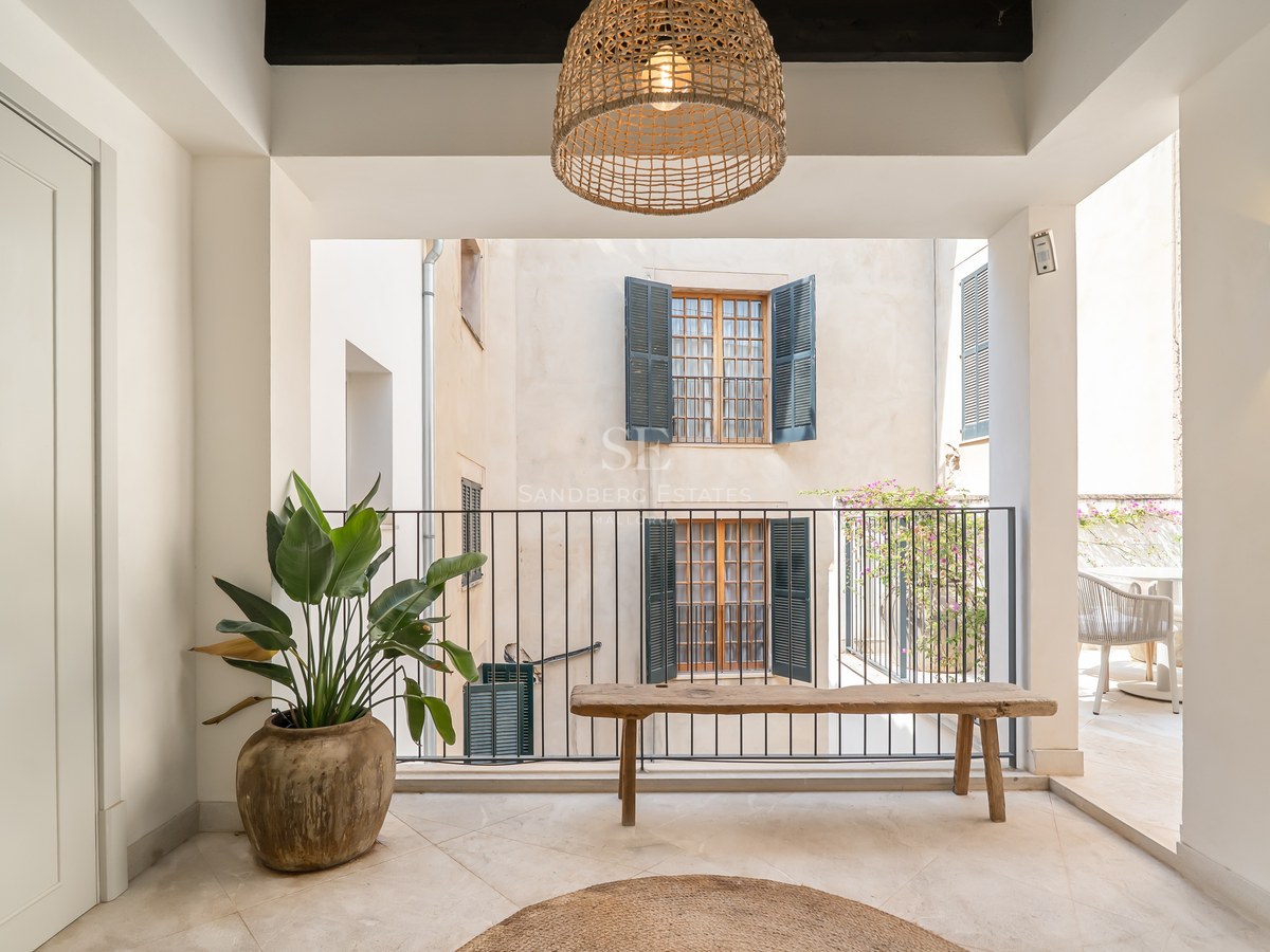 Covered terrace featuring a rustic wooden bench, large clay planter, and views of a traditional courtyard with shutters.