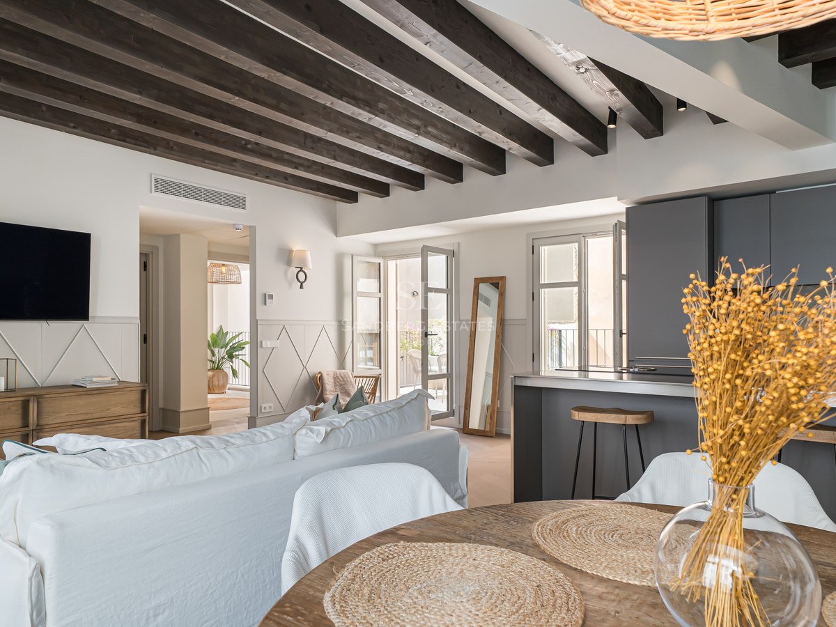 Open-plan living room with dark wood ceiling beams, a white linen sofa, and a modern charcoal grey kitchen.
