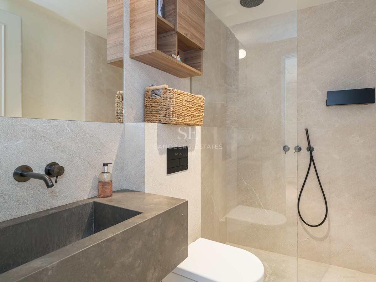 Modern bathroom with dark stone basin, wall-mounted black taps, and walk-in glass shower with beige stone tiles.