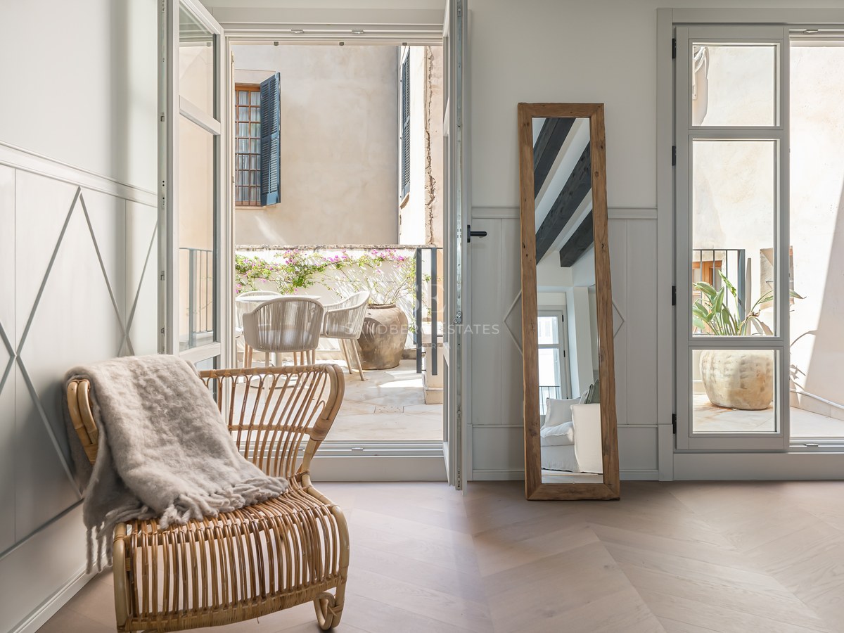 Interior room with chevron wood floors and open glass doors leading to a sun-drenched stone terrace.