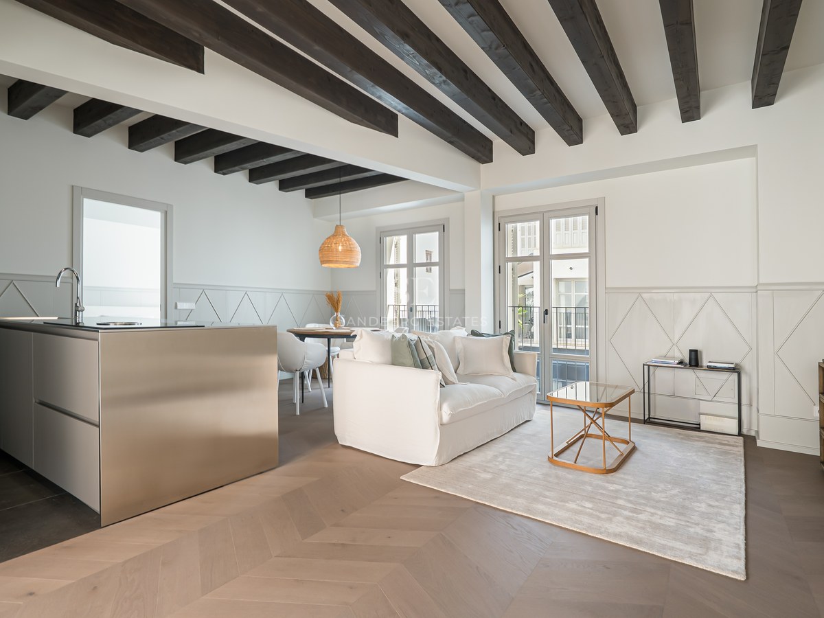 Modern living room with dark wood ceiling beams, chevron floors, and a sleek stainless steel kitchen island.