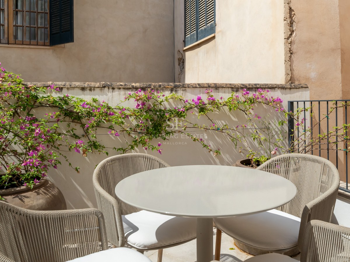 A round grey outdoor table and four woven chairs on a sun-drenched terrace with vibrant pink bougainvillea.