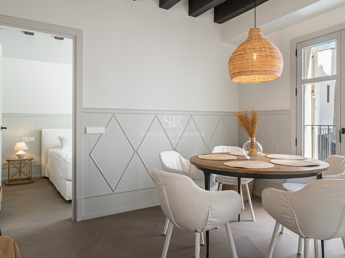 Modern dining room with round wooden table, white chairs, and woven pendant light next to a bedroom entrance.