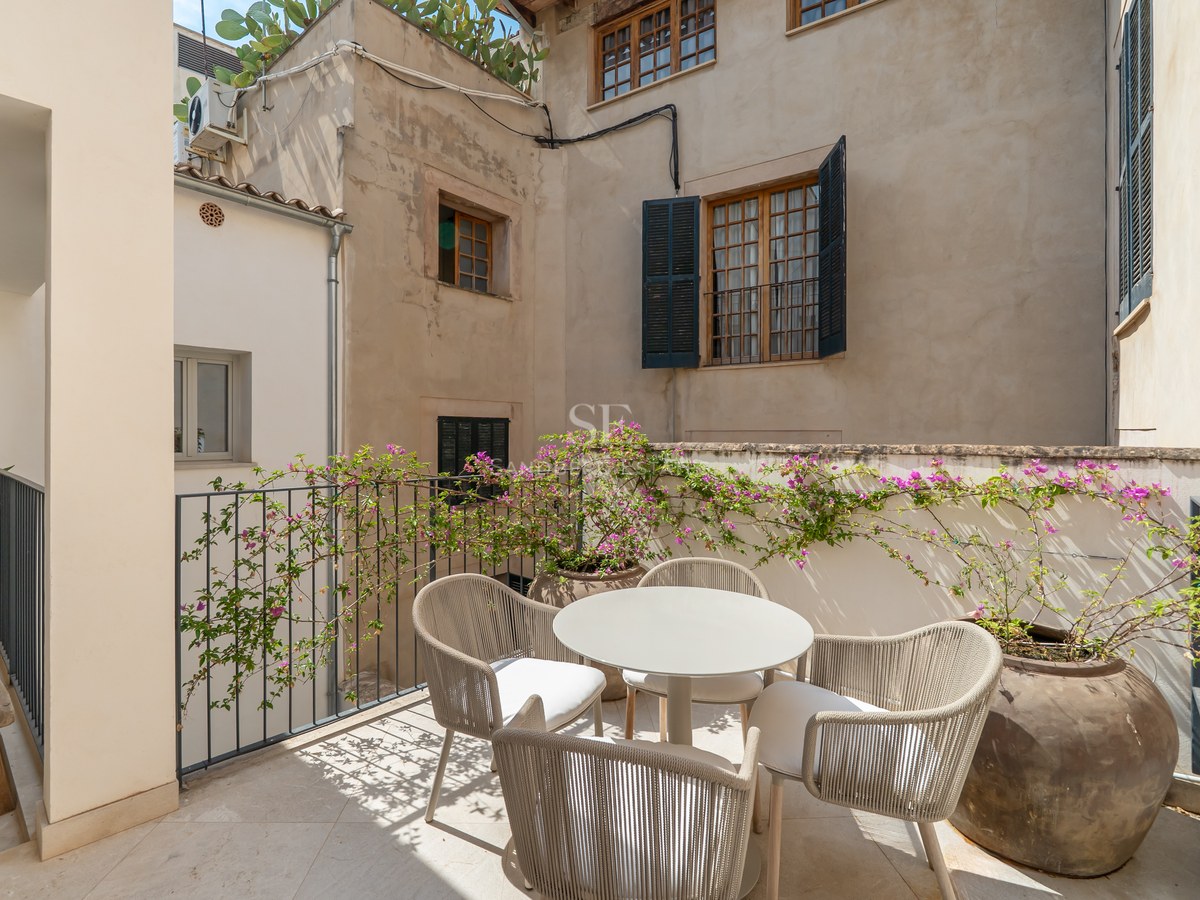 Sunlit terrace with modern outdoor dining set, surrounded by traditional stone walls, shutters, and flowering bougainvillea.