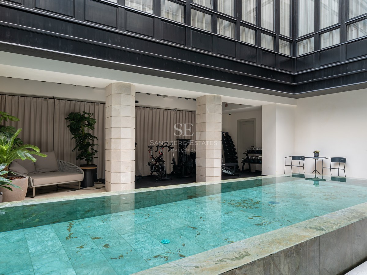 Heated indoor swimming pool with turquoise tiling adjacent to a private gym area with spin bikes and weights.