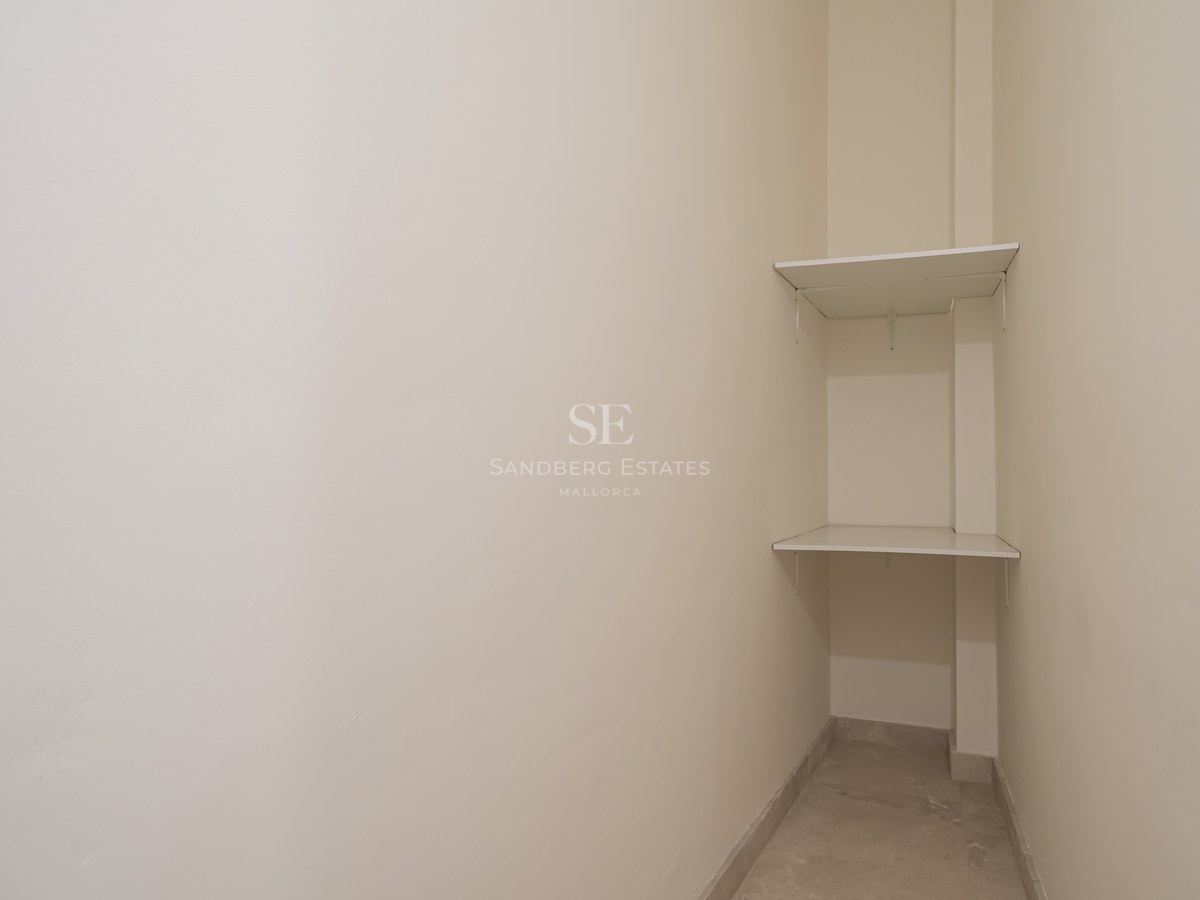 A small corner storage space featuring two white shelves against cream-colored walls and light tiled flooring.