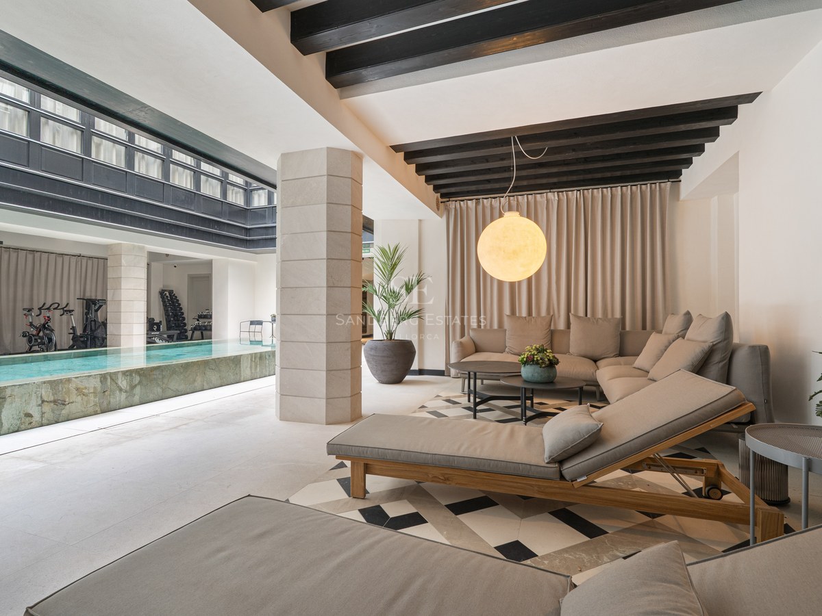 Relaxation lounge with sofas and daybeds next to an indoor lap pool with a fitness area in the background.