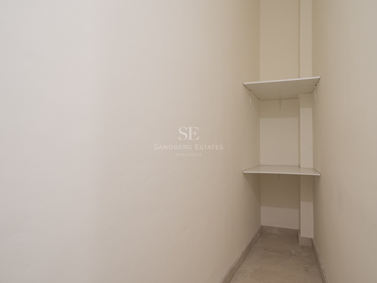 Narrow off-white storage area with two white shelves in a corner and light stone flooring.