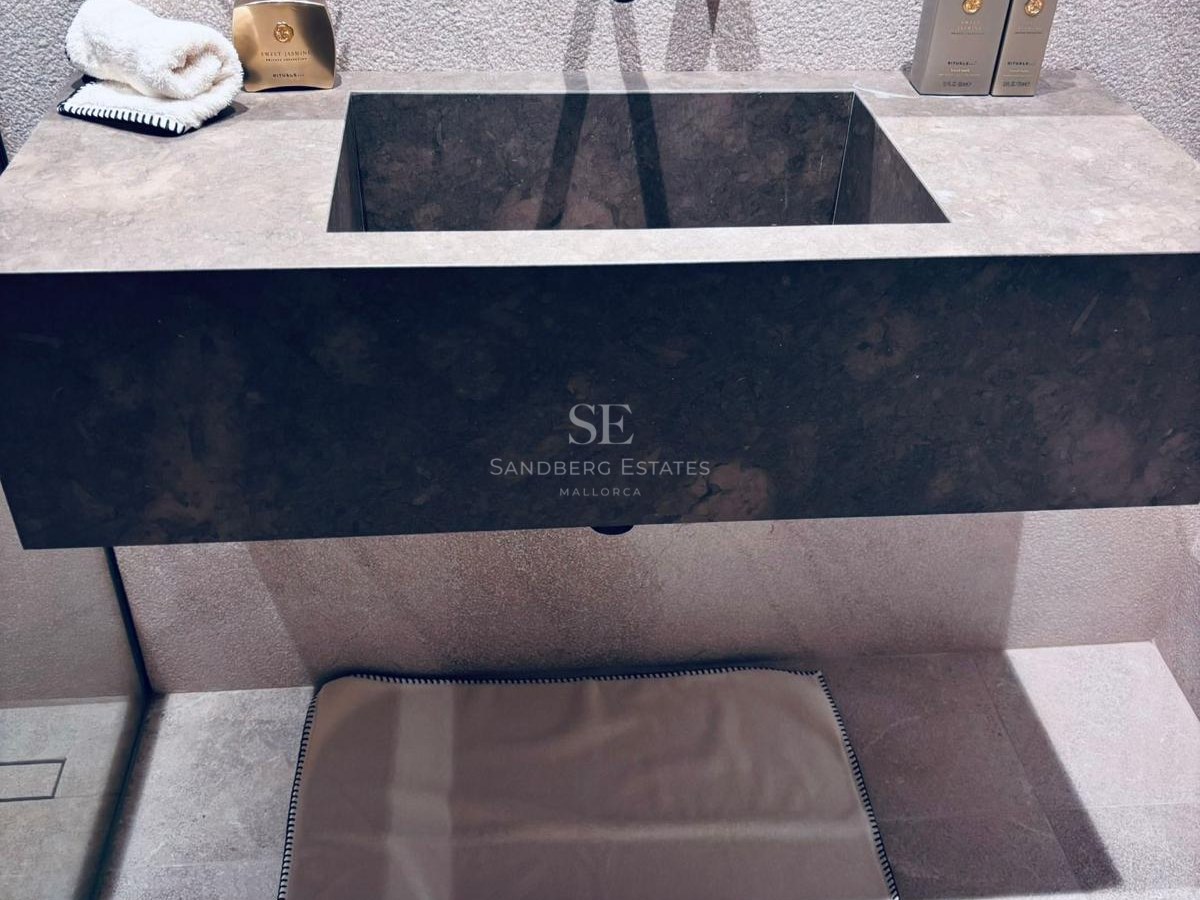 Close-up of a dark natural stone floating sink with matte black wall-mounted taps and textured stone walls.
