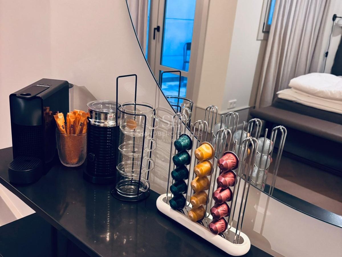 Black console with a Nespresso machine, milk frother, and capsule holder reflected in a round mirror.