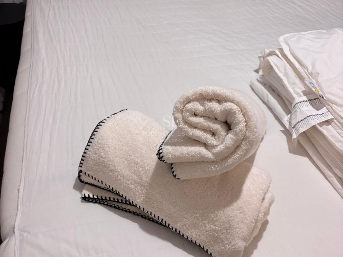 Close-up of a bed with white quilted duvet and plush towels featuring black stitched edges in a modern bedroom.