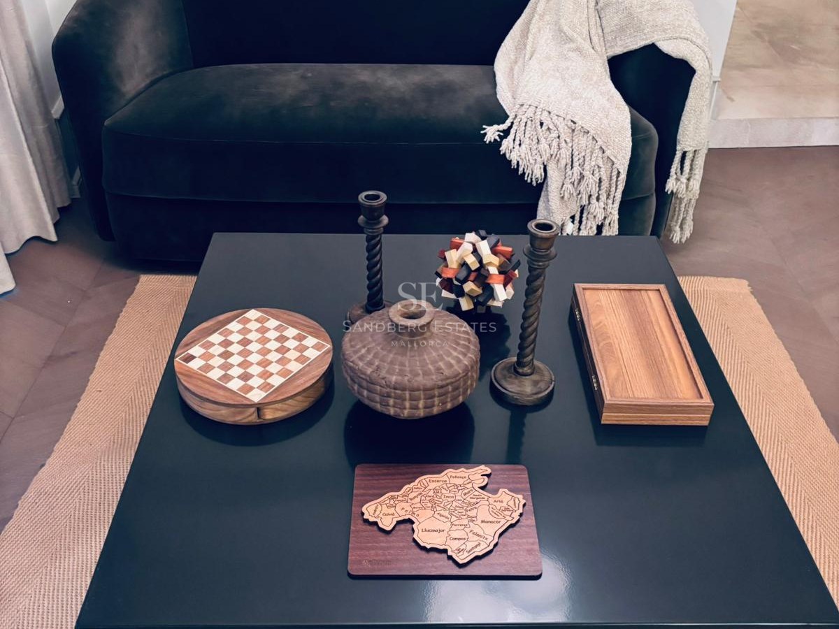A black square coffee table featuring wooden decorative items including a Mallorca map and chess set.
