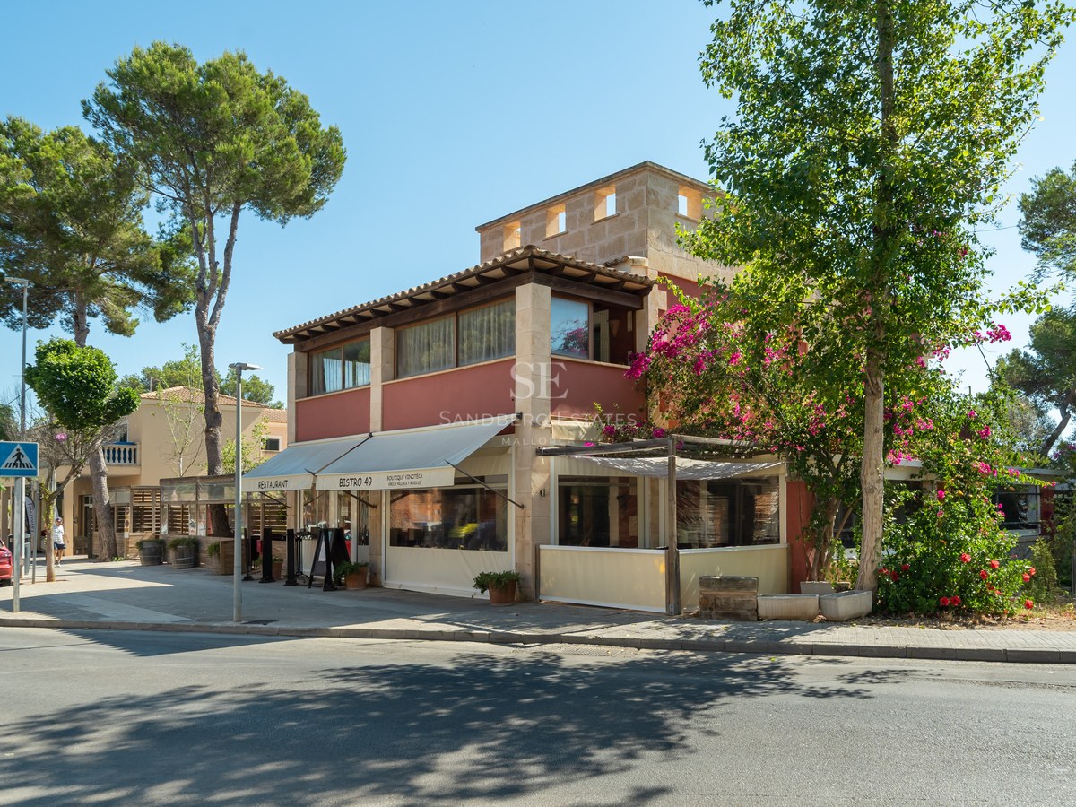Edificio mediterráneo de dos plantas con un restaurante en la planta baja, rodeado de pinos y buganvillas.