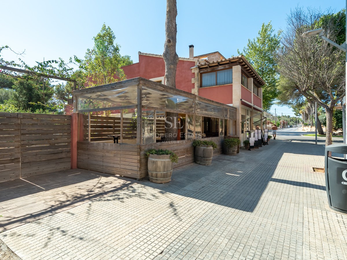 Fachada de edificio terracota con terraza de madera cerrada en una acera soleada de Calvià.