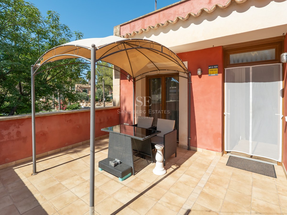 Terraza soleada con paredes de color terracota, suelo de baldosas y un cenador con mesa y sillas.