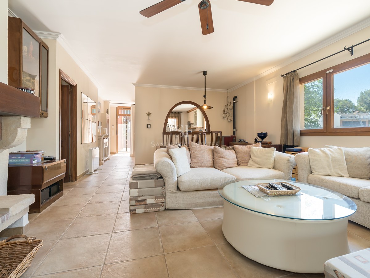 Salón acogedor con suelos de terracota, sofás crema, mesa de centro de cristal y chimenea de leña.
