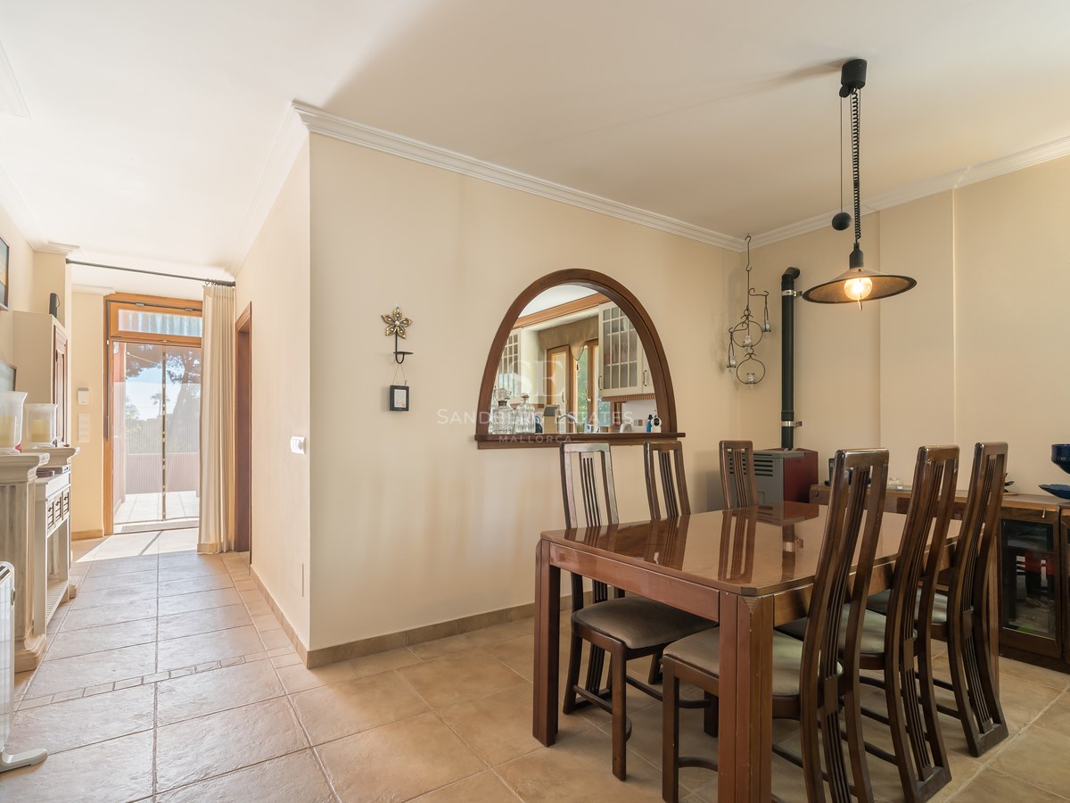 Comedor con mesa de madera oscura, suelos de terracota y un arco con vista a la cocina en una villa luminosa.