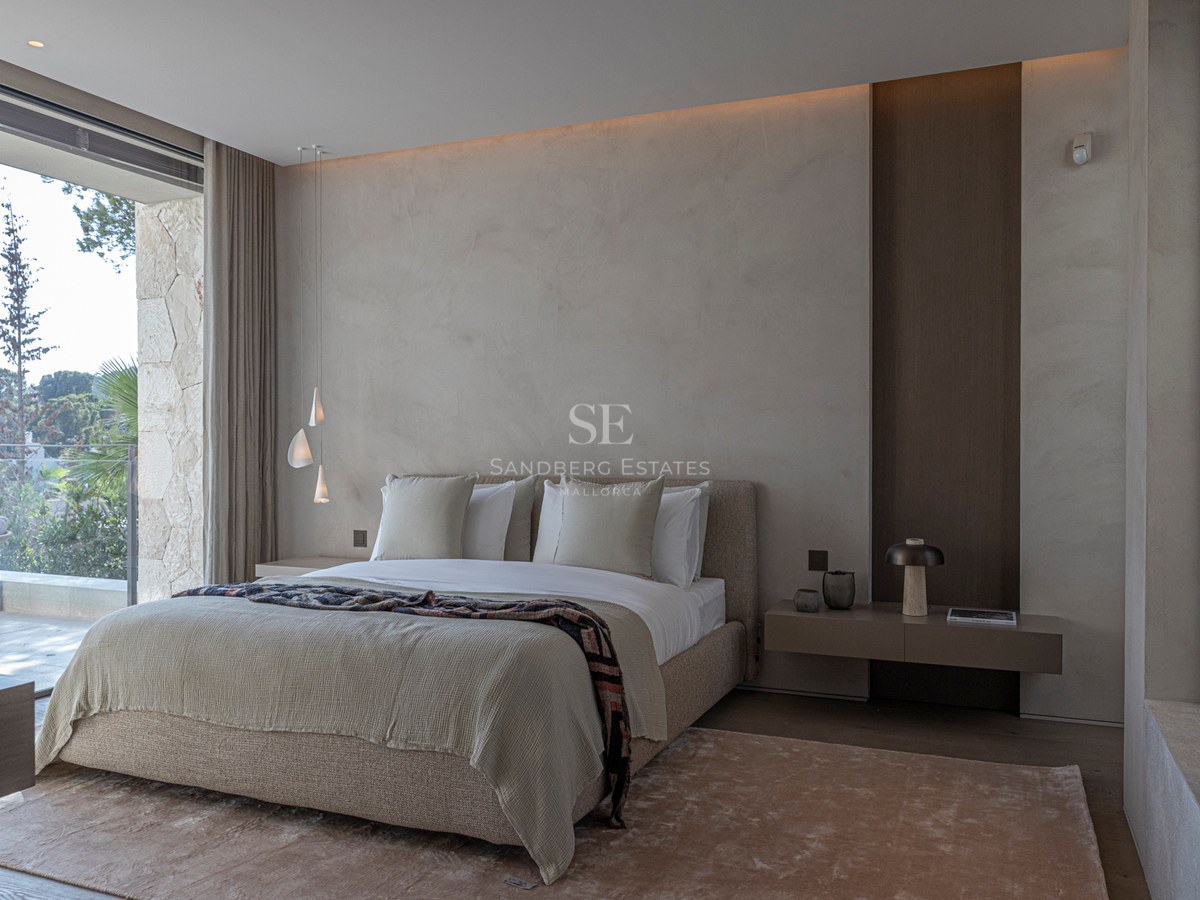 Chambre principale moderne, tons neutres, murs texturés, grandes baies vitrées donnant sur une terrasse en pierre.