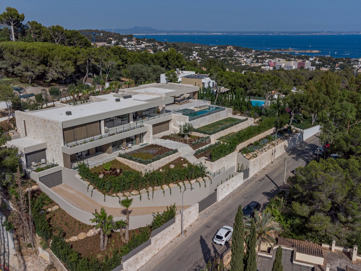 Vue aérienne d'une villa contemporaine à plusieurs niveaux avec murs en pierre naturelle, piscine à débordement et vue mer.