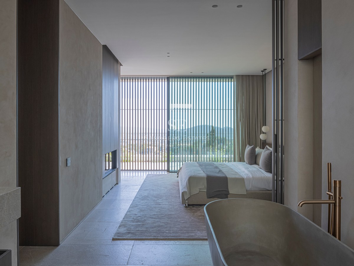 Chambre principale moderne avec baignoire en pierre, baies vitrées avec persiennes en bois et cheminée.