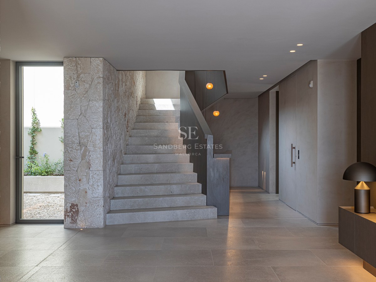 Couloir moderne avec escalier en pierre, murs en pierre texturée et éclairage design chaleureux.