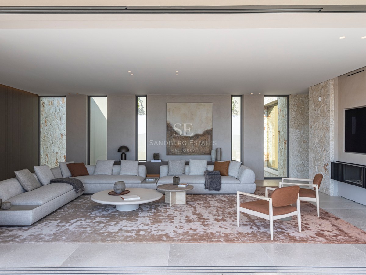 Un salon spacieux et moderne avec des canapés gris, un mur en pierre naturelle et de grandes baies vitrées.