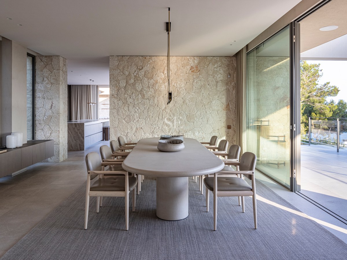 Salle à manger contemporaine avec table ovale en pierre, mur en pierre naturelle et grandes baies vitrées.