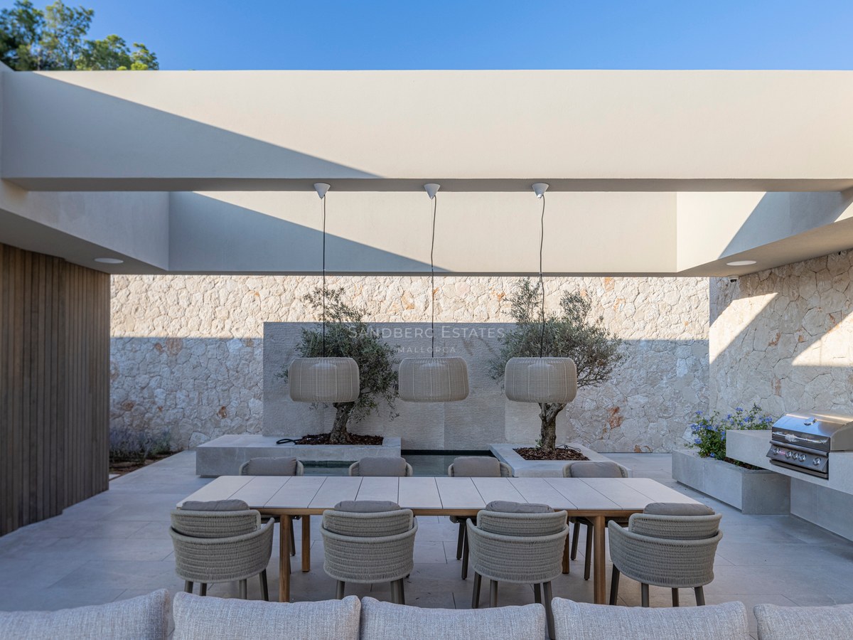 Terrasse moderne avec une grande table en bois, des chaises tressées, des suspensions design et un barbecue intégré.