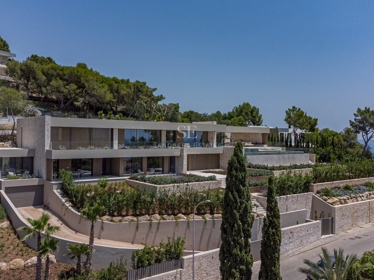 Villa moderne sur plusieurs niveaux sur une colline avec murs en pierre, garde-corps en verre et jardins méditerranéens.