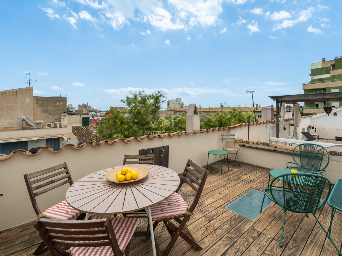 Terraza de madera en azotea con mesa de comedor, sillas de metal verde y vistas panorámicas de Palma y la catedral.