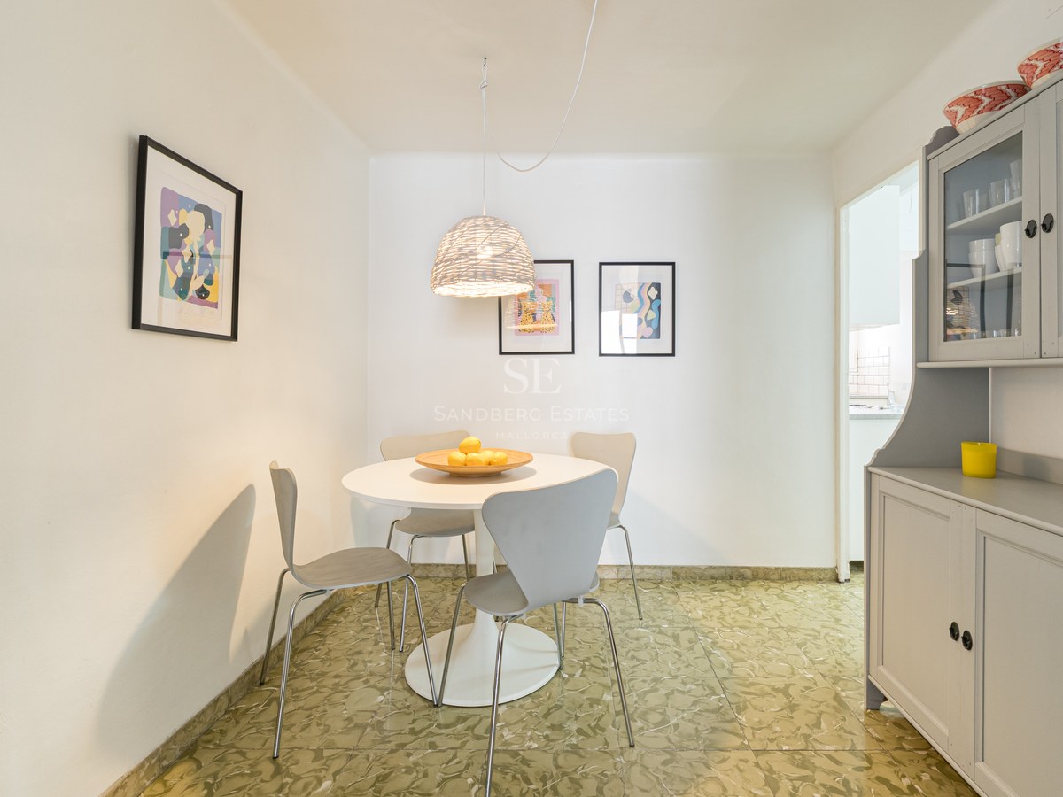Zona de comedor luminosa con mesa redonda blanca, sillas grises modernas y suelo de baldosa verde estampada.
