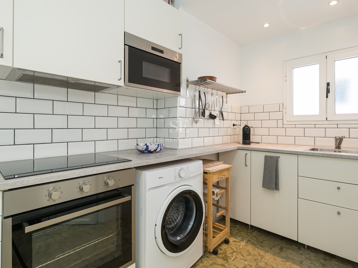 Cocina blanca moderna con azulejos tipo metro, horno integrado, placa de inducción y lavadora bajo encimera.