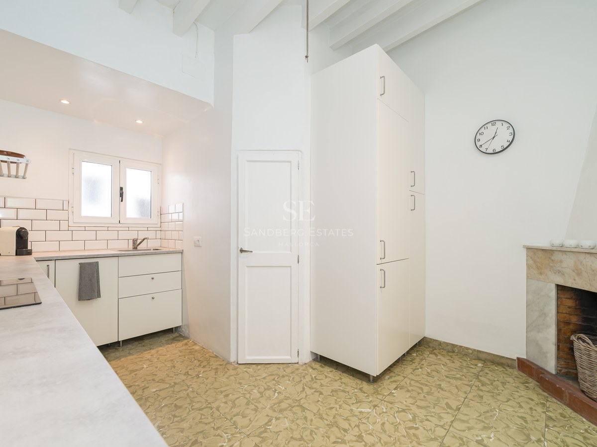 Cocina blanca moderna con chimenea de mármol, techos de vigas vistas y suelos decorativos.