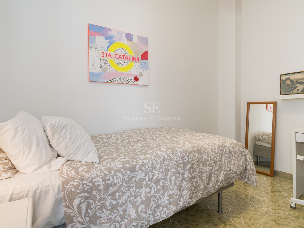 Dormitorio individual luminoso con cama estampada, escritorio blanco y suelo hidráulico tradicional.