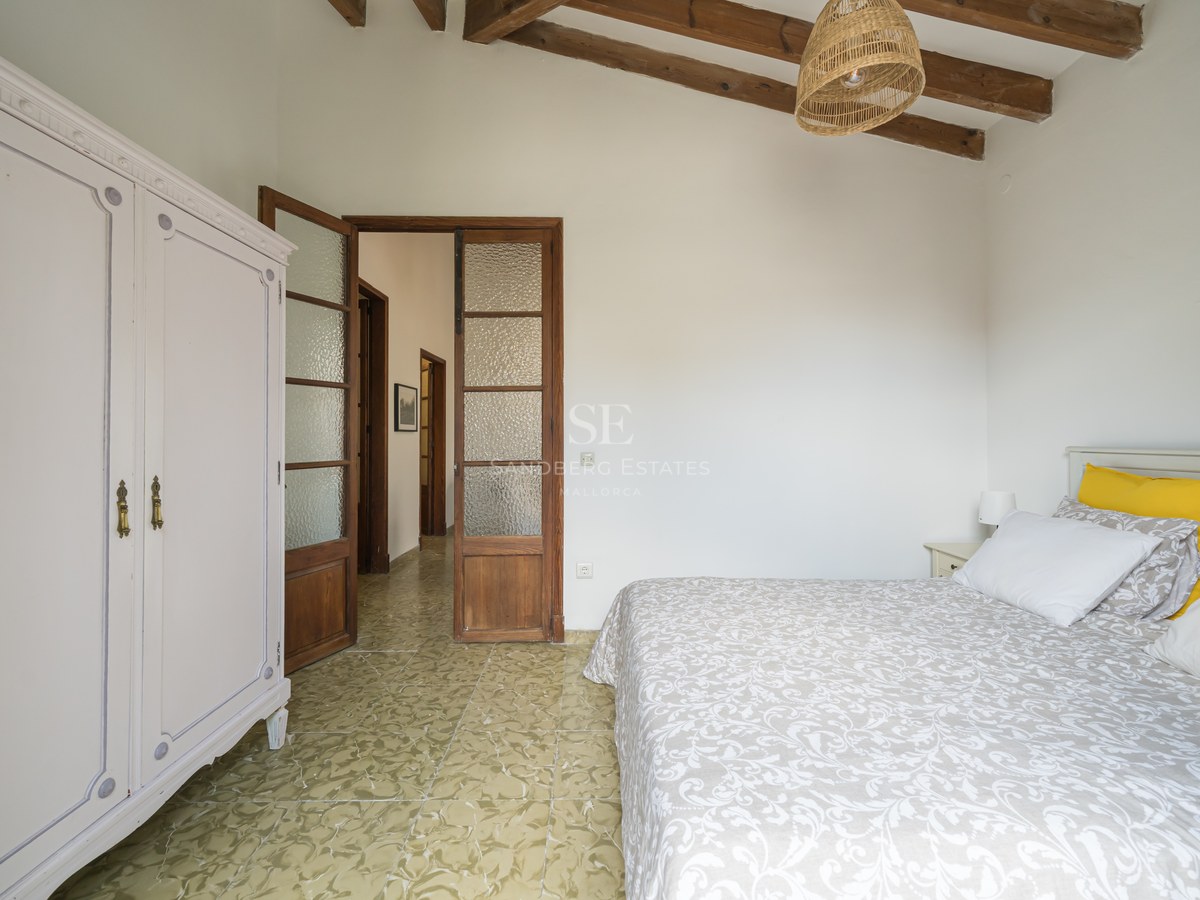 Dormitorio con vigas de madera en el techo, suelo de baldosas verdes estampadas, armario blanco y puertas rústicas.