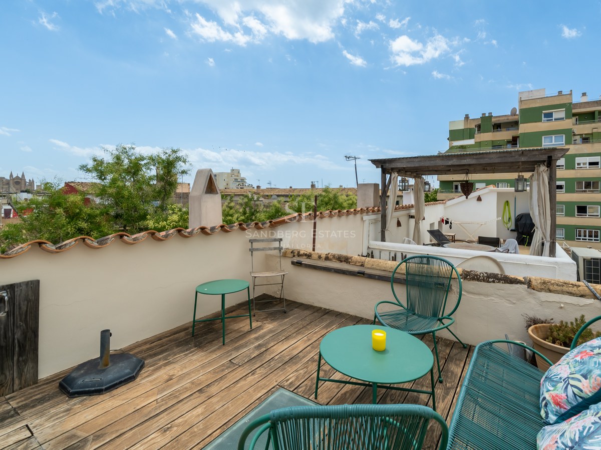Terraza en azotea con suelo de madera, muebles verde azulado y vistas a la Catedral de Palma.