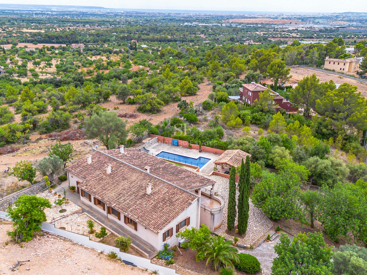 Vue plongeante d'un grand domaine avec une villa au toit de terre cuite, une piscine bleue et un cadre verdoyant.
