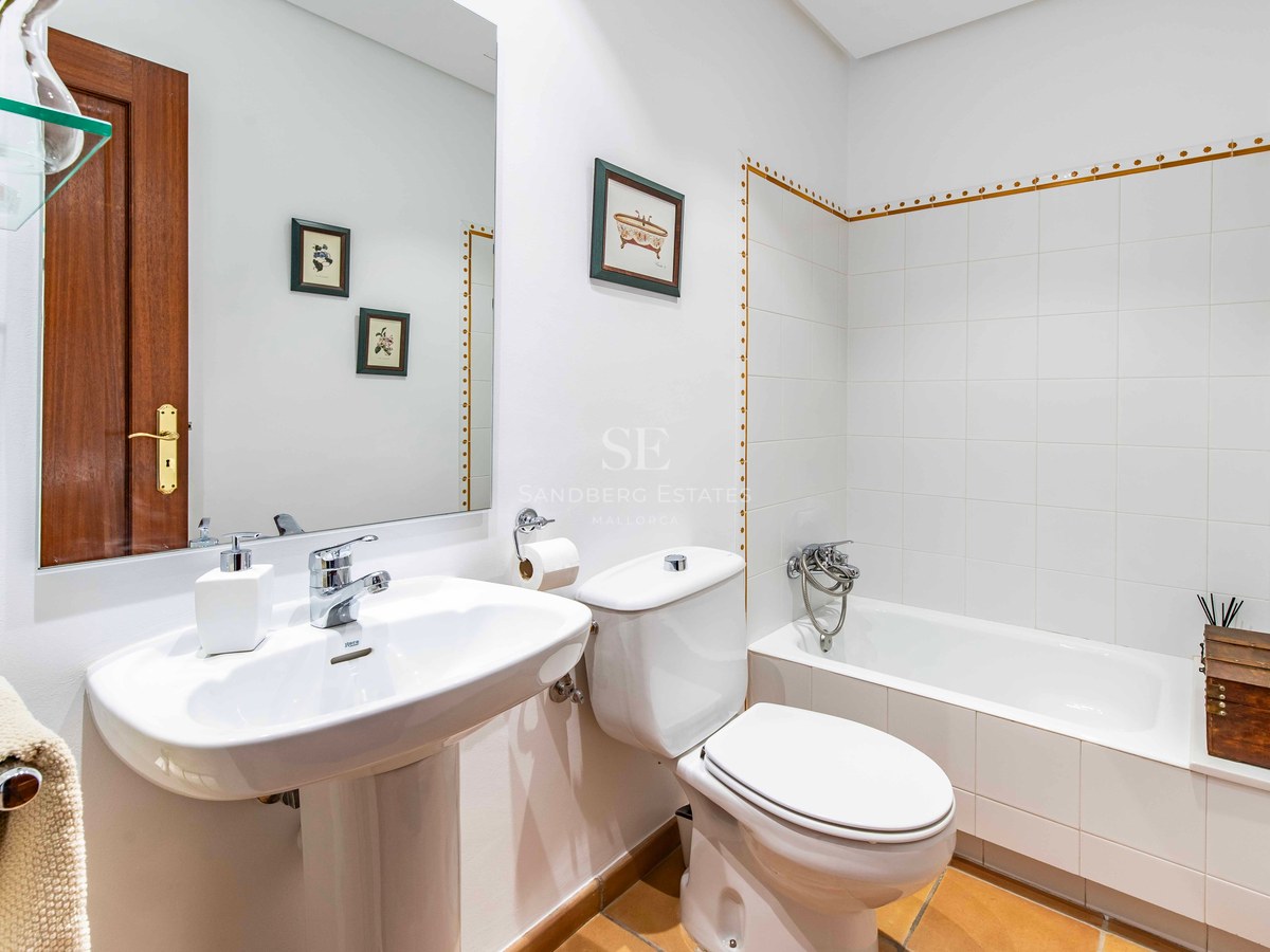 Salle de bain avec carrelage blanc, baignoire, lavabo colonne, toilettes et sol en terre cuite.