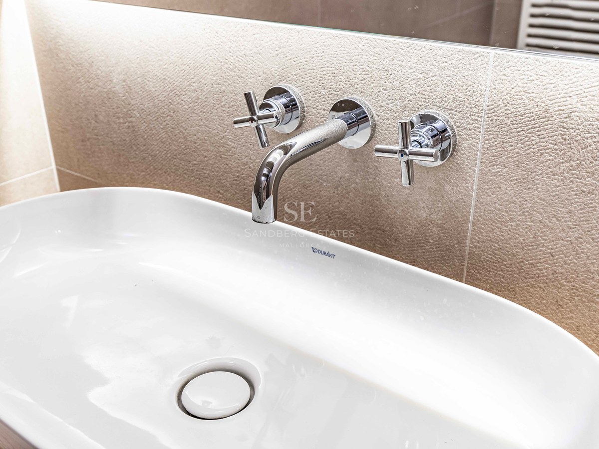 Närbild på ett vitt Duravit-tvättställ med väggmonterad kromad blandare mot en texturerad stenvägg.