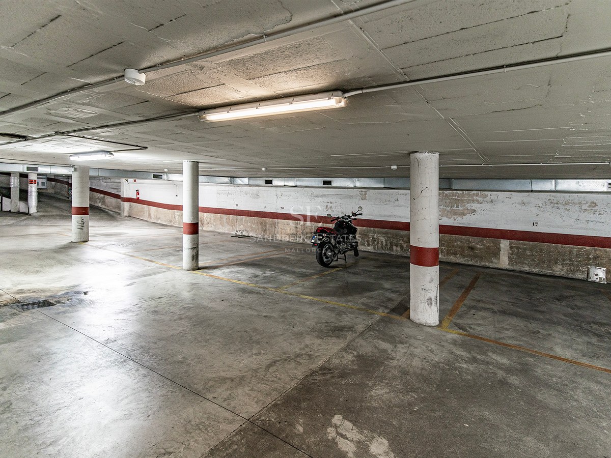 Underjordiskt betonggarage med numrerade parkeringsplatser, pelare och en parkerad motorcykel.