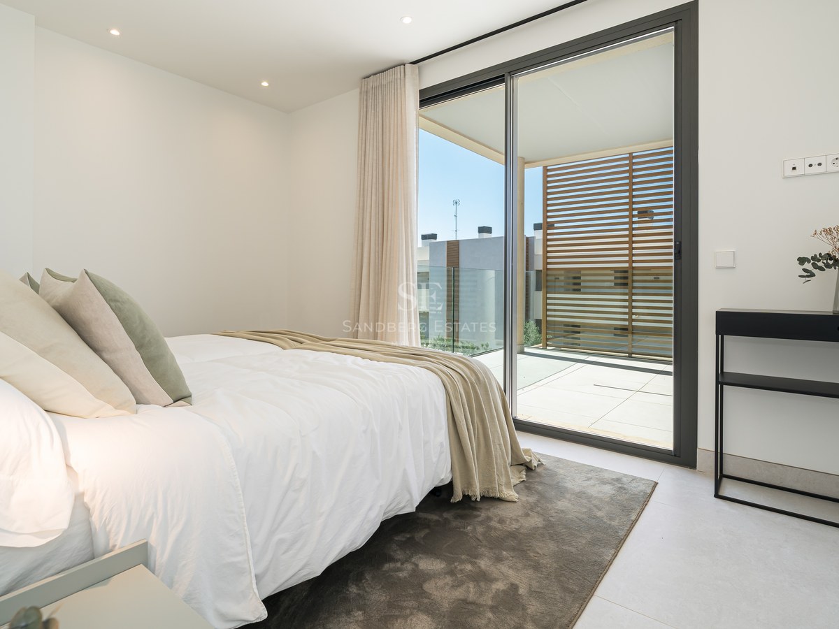 Contemporary bedroom featuring a white bed, black console table, and sliding glass doors leading to a sunny terrace.