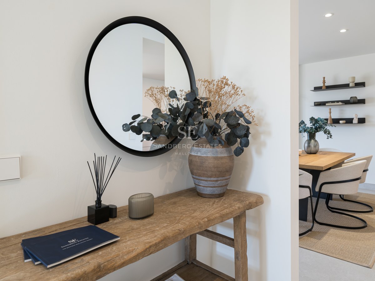Minimalist entryway featuring a rustic wooden console table, round black mirror, and view into a modern dining room.