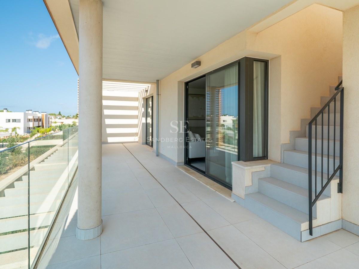 Spacious sun-drenched terrace with large format tiles, a glass railing, and outdoor stairs leading to an upper level.