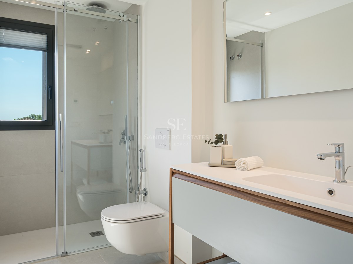 Bright bathroom featuring a glass walk-in shower, wall-mounted toilet, and white vanity with wood trim.