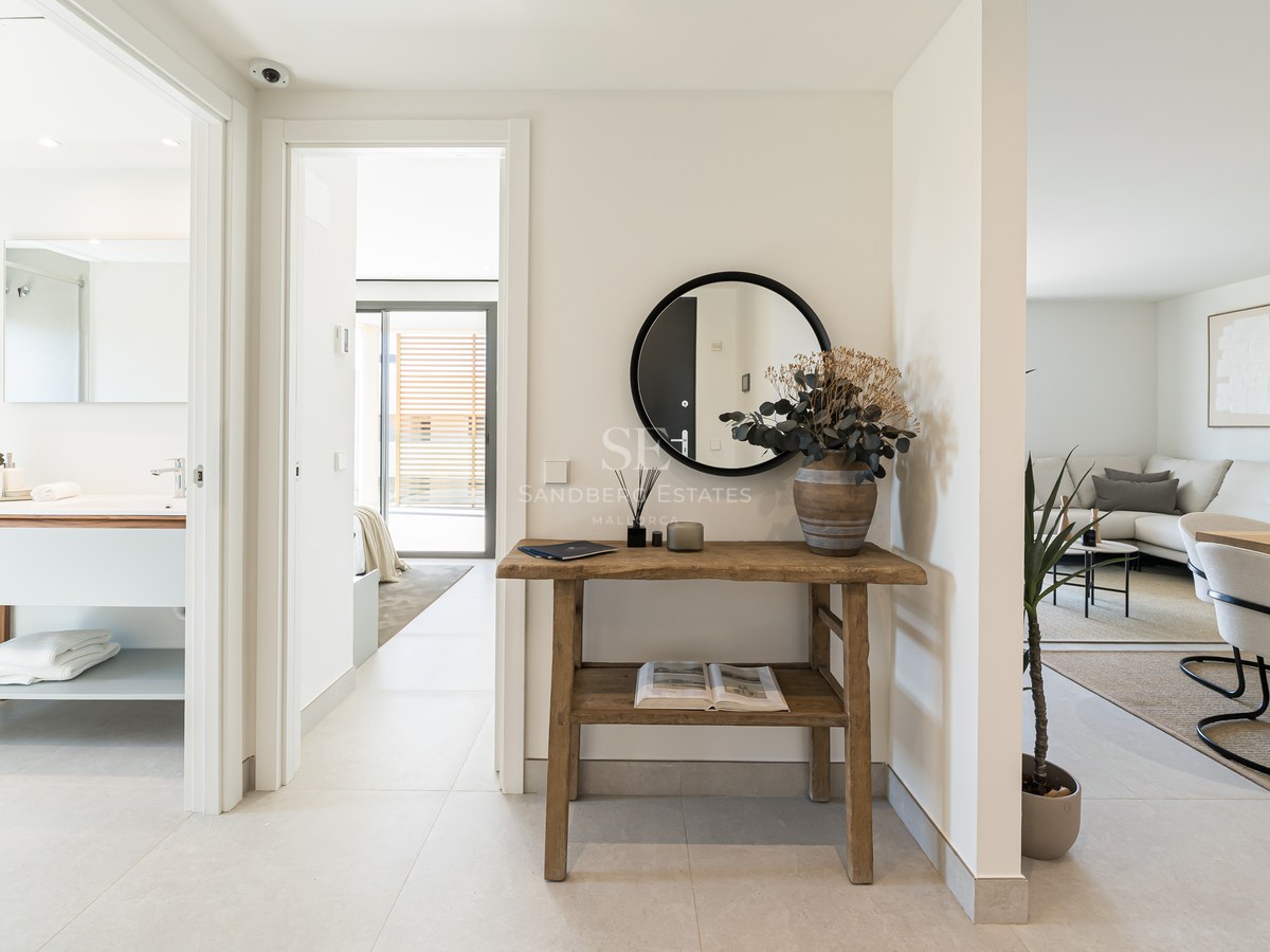 Bright hallway featuring a rustic wood console, round mirror, and views into a modern bathroom and living area.