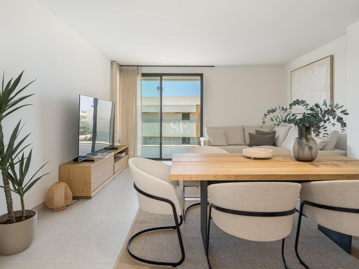 Bright open-plan room featuring a light wood dining table, cream chairs, a sectional sofa, and glass terrace doors.
