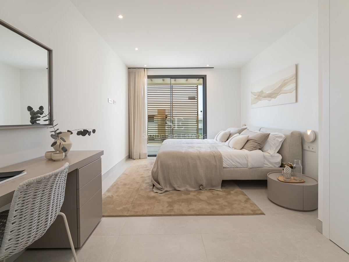 Bright modern bedroom with a large bed, integrated desk, floor-to-ceiling windows with wooden shutters, and neutral tones.