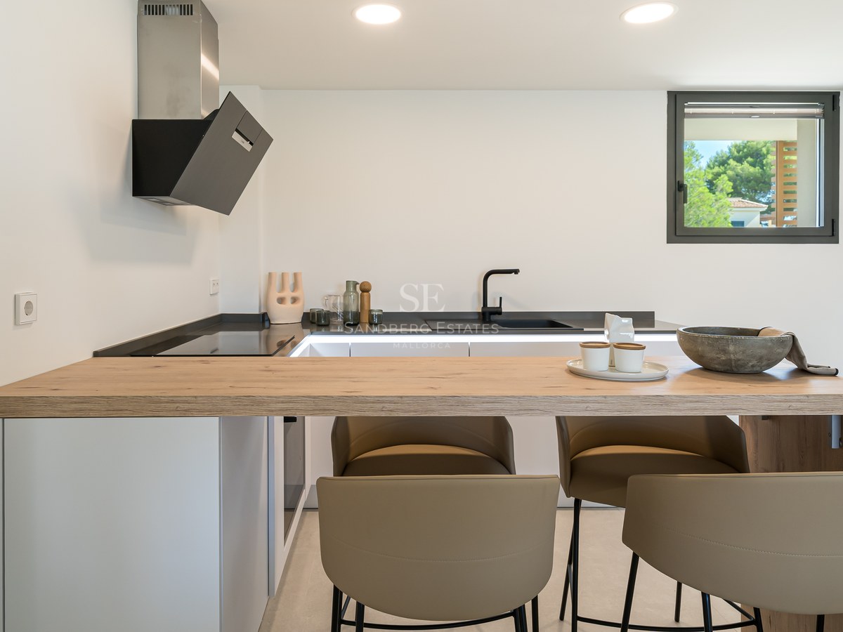 Contemporary white kitchen featuring a natural oak breakfast bar, black fixtures, and designer bar stools.