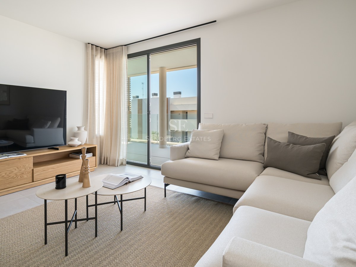 Bright living room featuring a cream L-shaped sofa, oak media unit, and sliding glass doors to a sunny terrace.